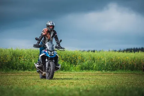 Jezdkyně stojí na stupačkách BMW R 1250 GS na louce pod bouřkovou oblohou