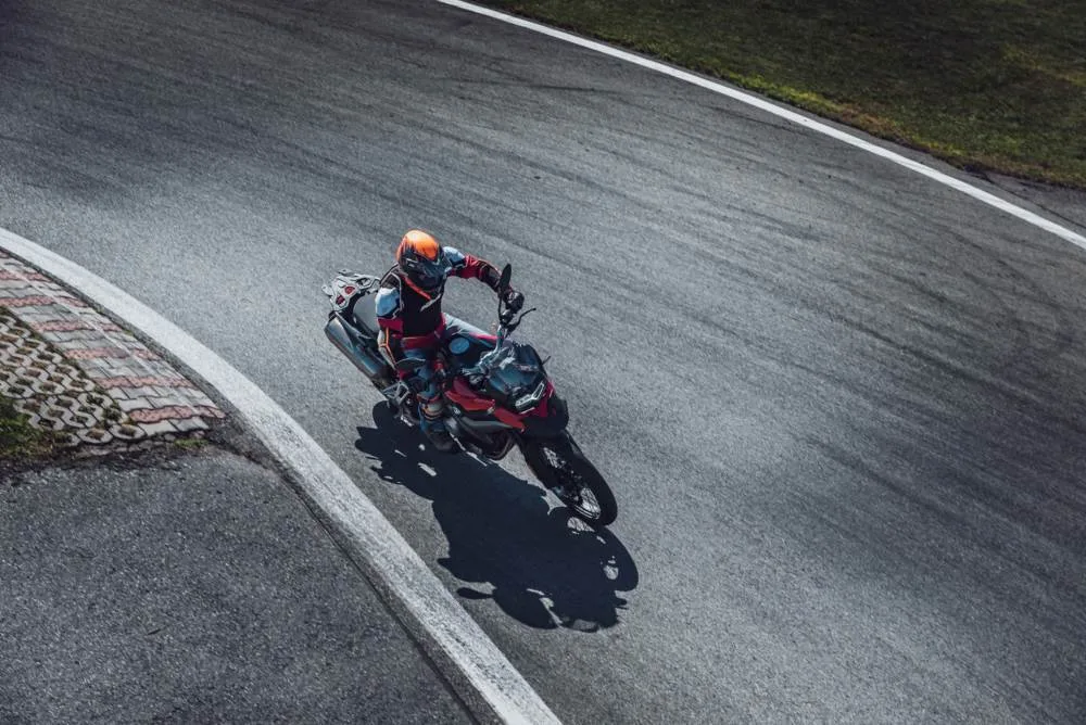 Pohled shora na jezdce naklánějícího BMW R 1250 GS v zatáčce závodního okruhu